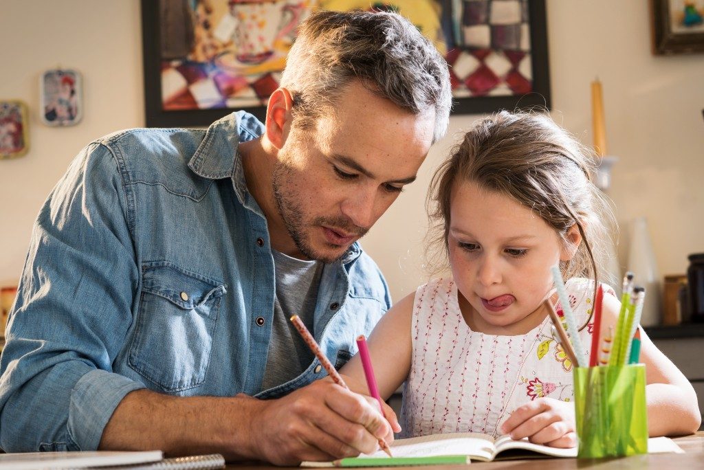 A father helps his little daughter to do her homework for the schoo