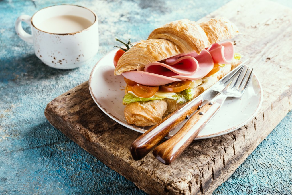 croissant sandwich with ham, cheese and salad leaf with coffee on blue table