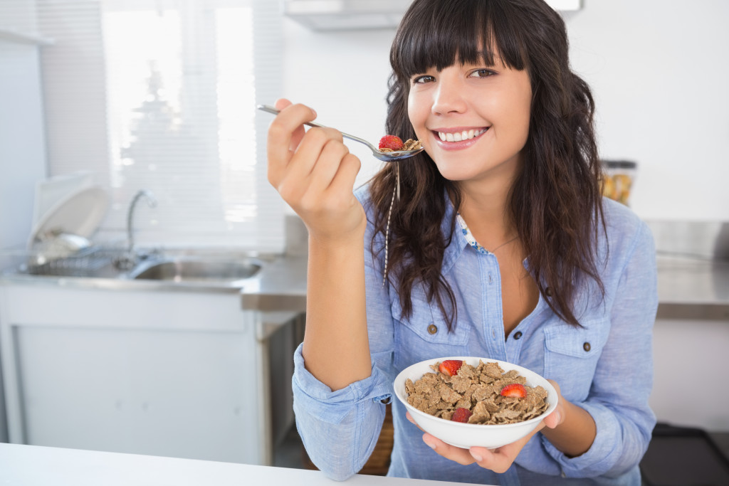 Woman eating a bowl of cereals with a fruit while inside an office.