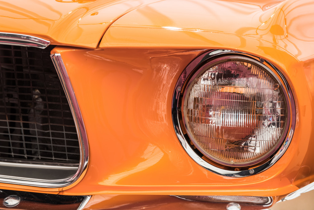 Headlight and part of the fender of an orange luxury car.