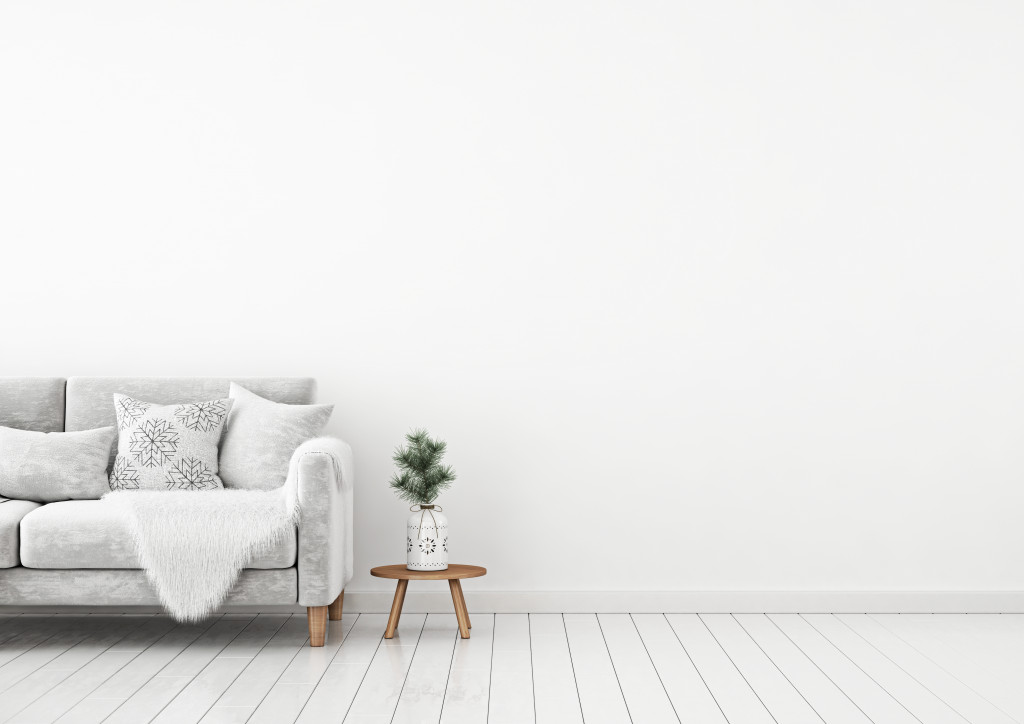 A white living room with a soft sofa, throw pillows, and fur blanket, and a potted plant