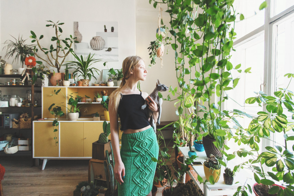 A woman holding er cat in a room filled with plants