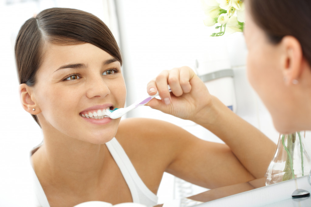 Image of pretty female brushing her teeth in front of mirror in the morning