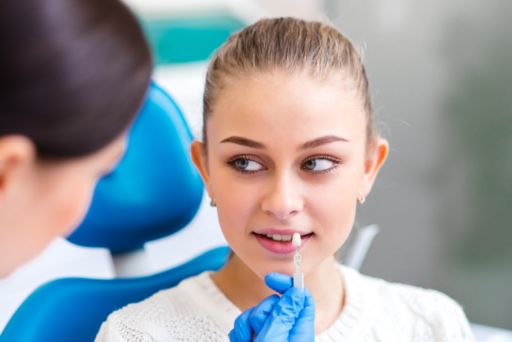 a woman smiling as a dentist uses artificial teeth to compare shades