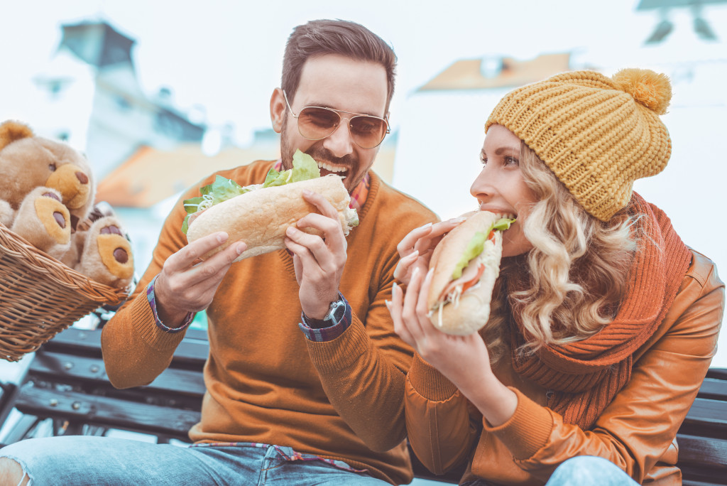 A couple eating sandwiches outdoors