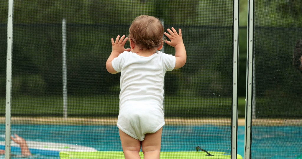 a baby leaning on a glass and steel safety gat by the pool