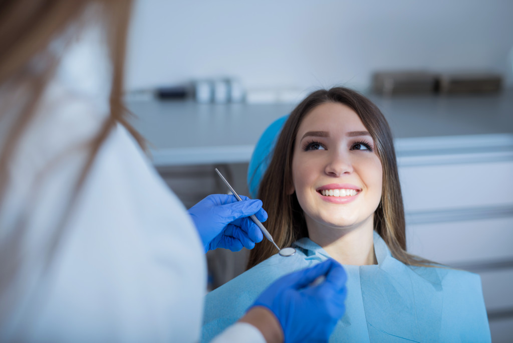 Smiling patient on a dentist's chair with the dentist in front of her using dental tools.